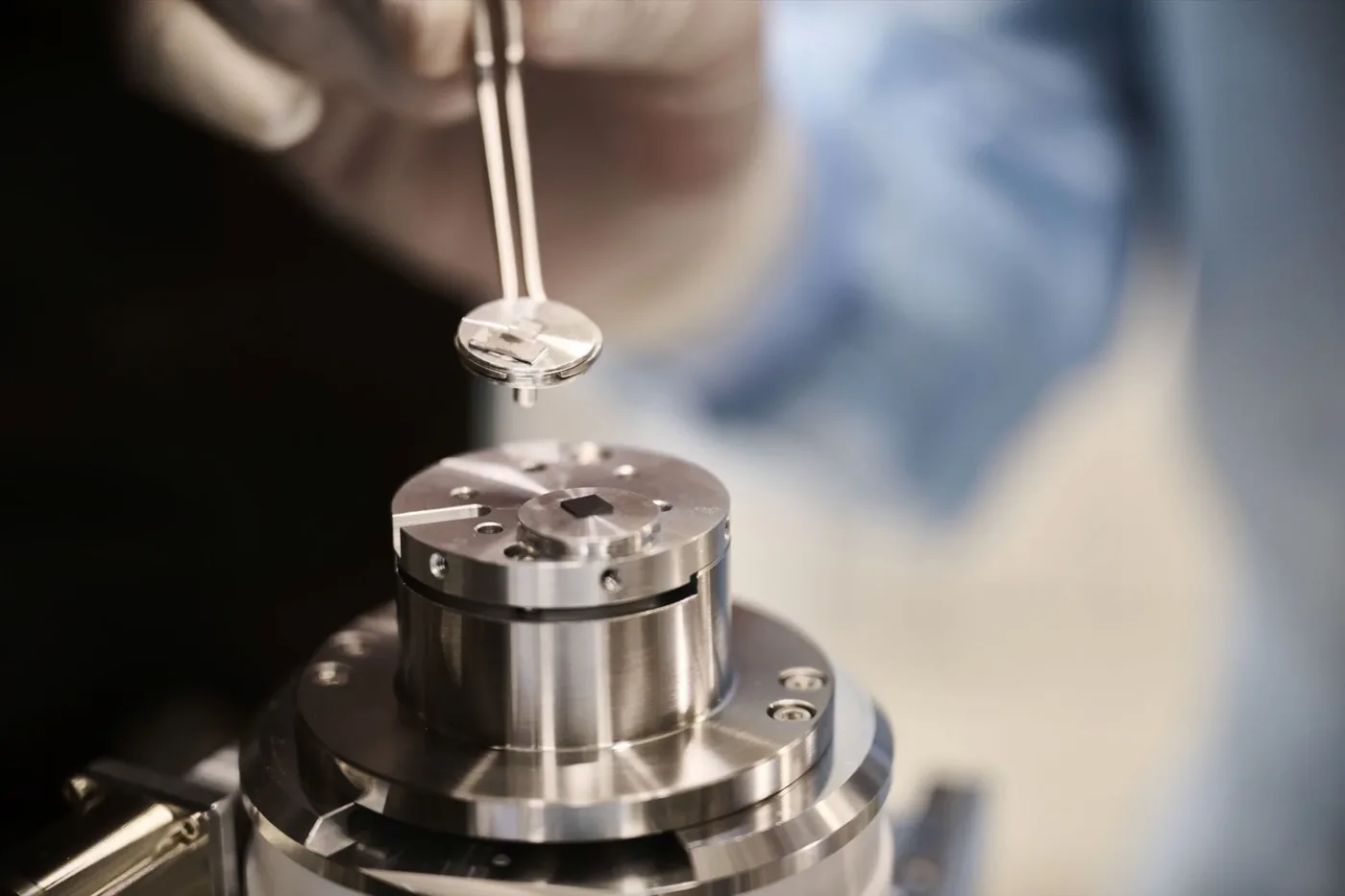 A diamond sample held with tweezers above laboratory hardware